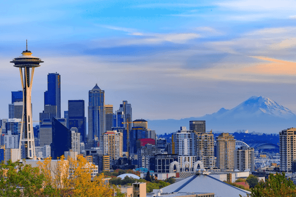 A city skyline with the space needle in the foreground and a mountain in the background.