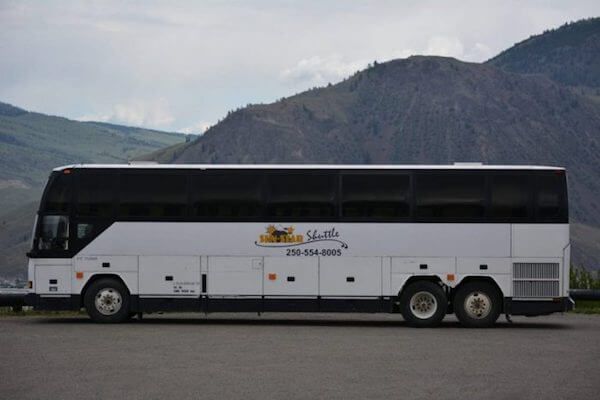 A white bus is parked in front of a mountain.