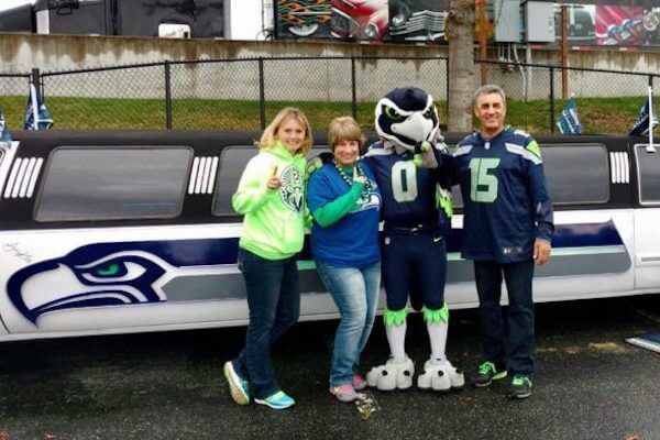A group of people standing in front of a seahawks limousine
