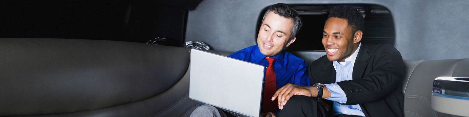 Corporate Car Services Seattle Two men are sitting in a car looking at a laptop.