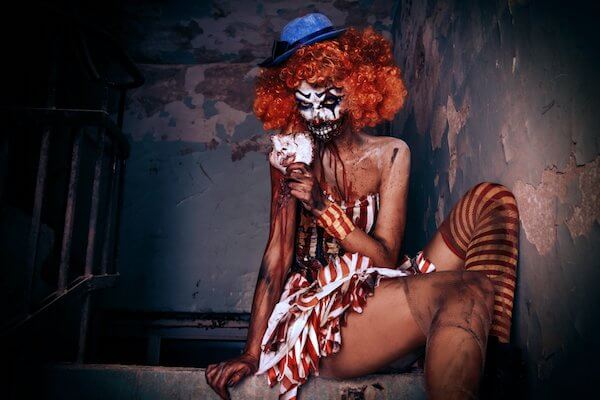 Halloween FreakFest limo services in Seattle A woman dressed as a clown is sitting on a ledge holding a playing card.