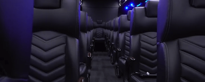 A row of black leather seats on a bus with purple lights.