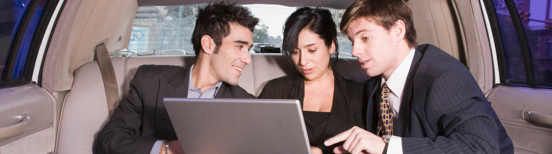 A group of people are sitting in a car looking at a laptop.