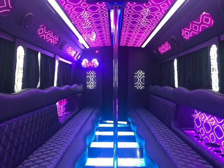 The inside of a limousine with purple lights and a pole.