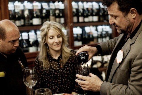 A man is pouring wine into a glass while a woman looks on.