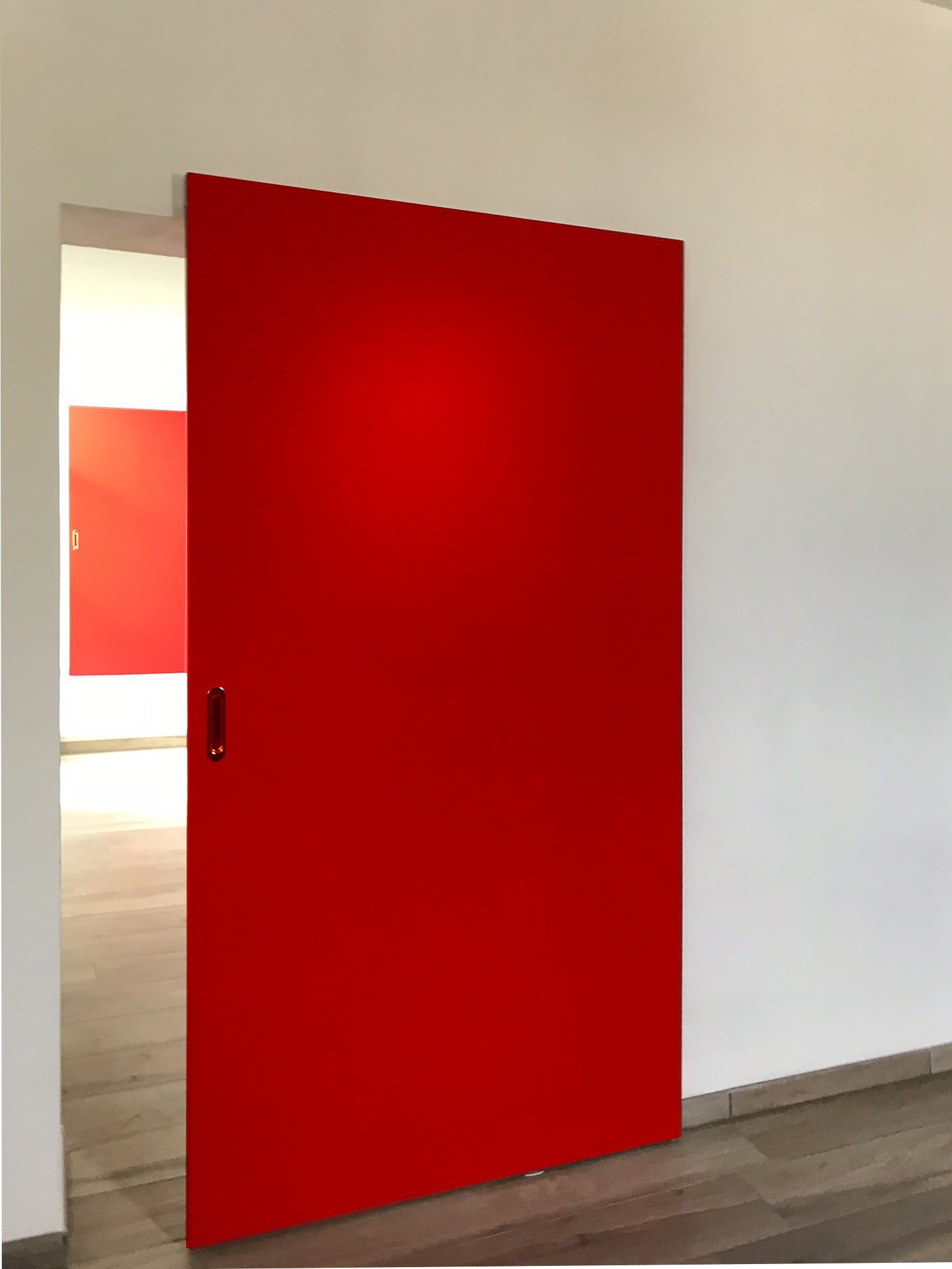 Una porta scorrevole rosso acceso è parzialmente aperta contro una parete bianca, rivelando un pannello rosso abbinato nella stanza retrostante.