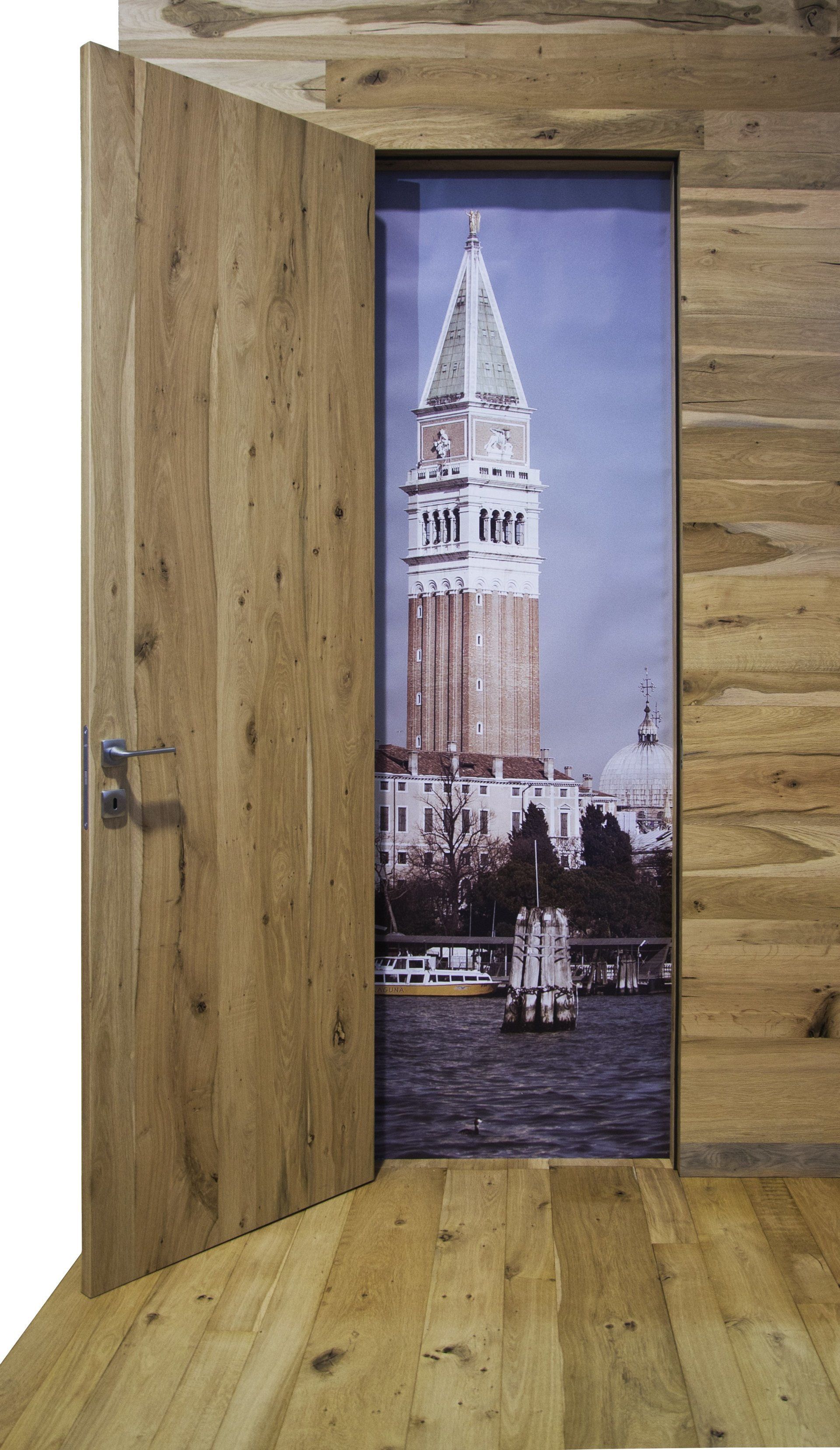 Una porta di legno chiaro è leggermente aperta, lasciando intravedere il Campanile di San Marco a Venezia.