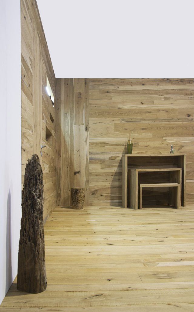 Una stanza minimalista con pareti e pavimento in legno chiaro, caratterizzata da un set di tavolini in legno impilabili e un tronco verticale rustico.