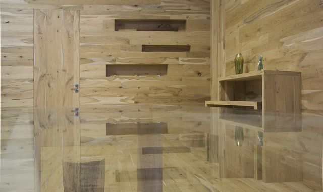 Una stanza moderna e minimalista con pareti rivestite in legno naturale, mensole a incasso, una porta nascosta e una consolle in legno.