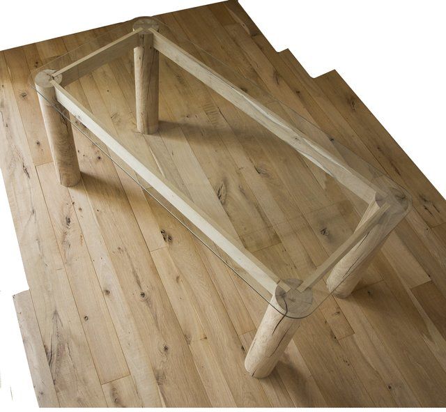 Un tavolino da caffè con piano in vetro e quattro gambe cilindriche in legno chiaro, poggiato su un pavimento in legno coordinato.