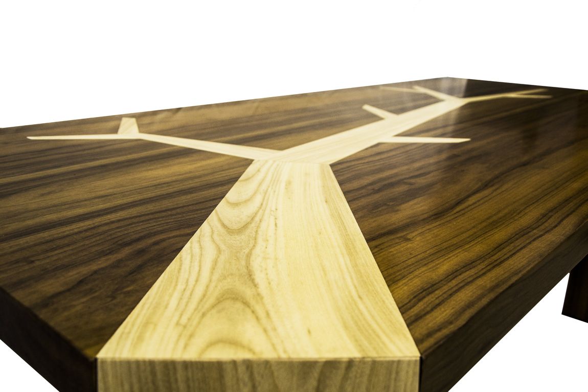 Primo piano di un tavolo di legno con un intarsio in legno chiaro a forma di ramo d'albero su una superficie di legno scuro.