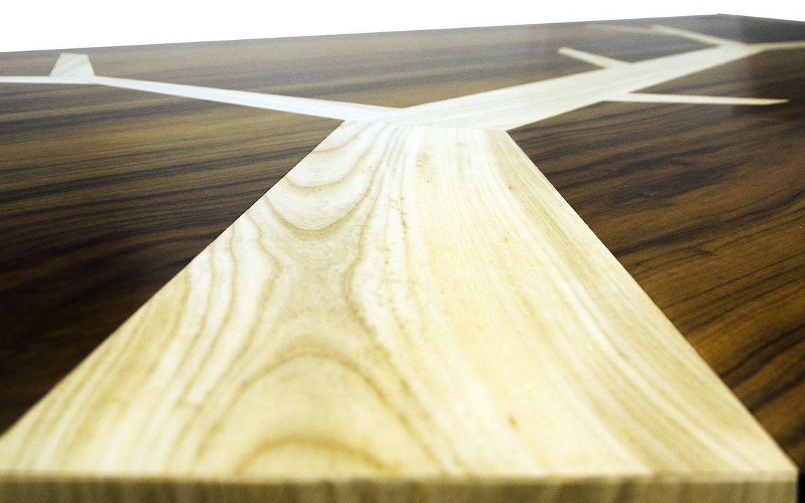 Primo piano di un tavolo in legno lucido con intarsio ramificato in legno chiaro su una base in legno scuro.