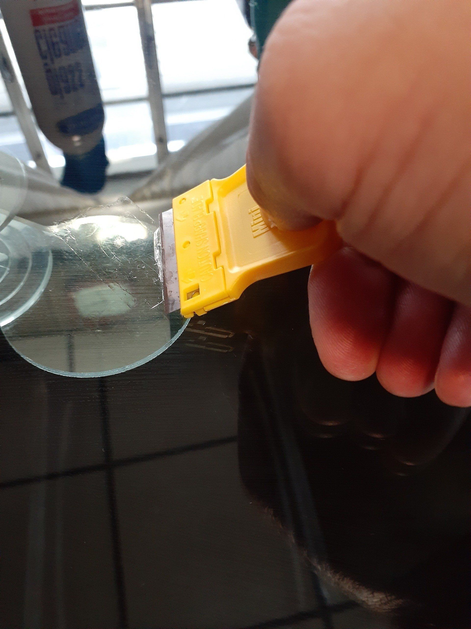 A person is holding a yellow scraper over a glass bottle