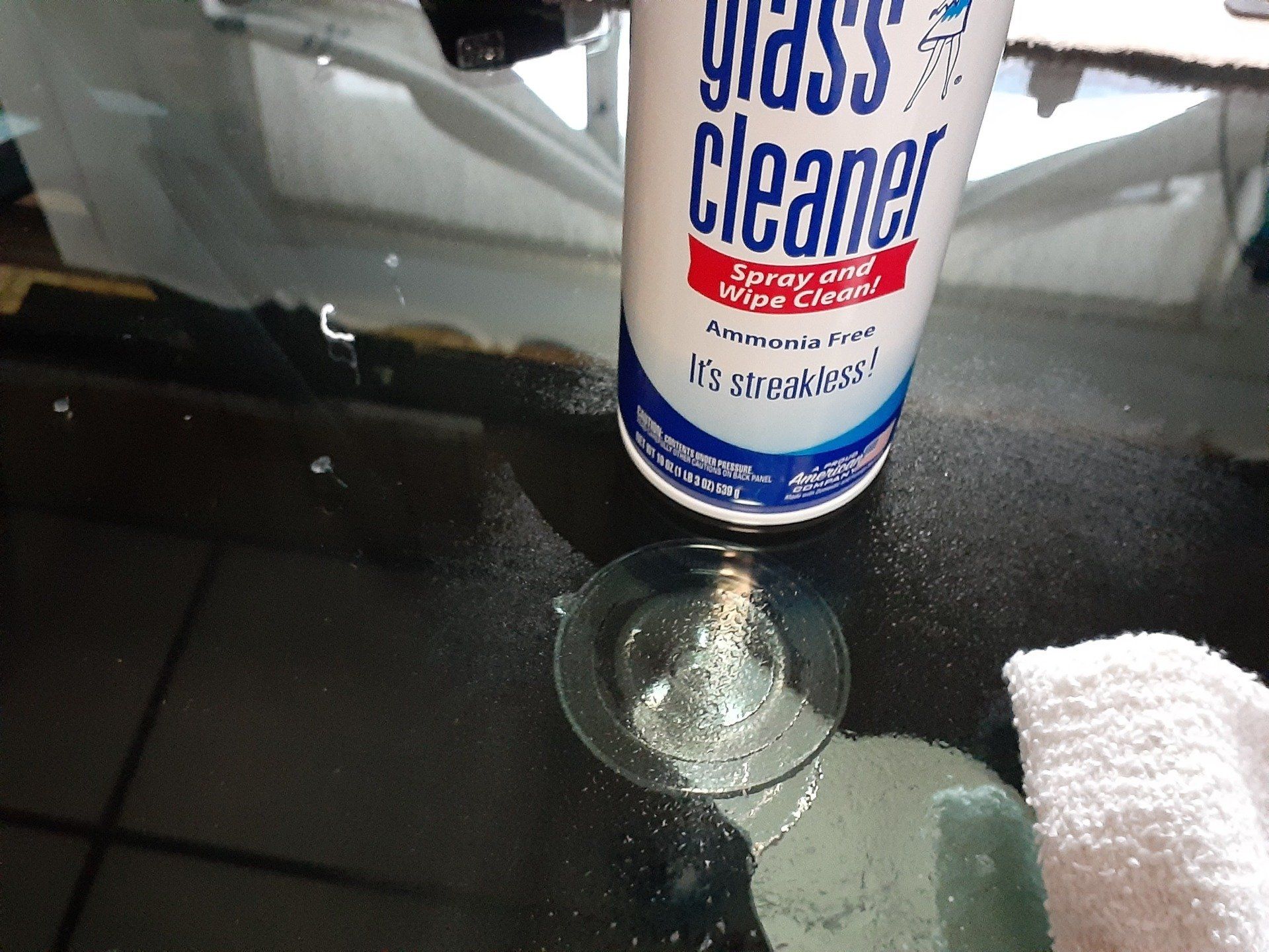 A bottle of glass cleaner sits next to a glass