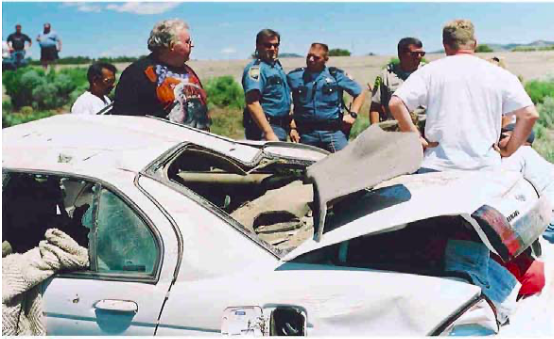 A group of men are standing around a wrecked car
