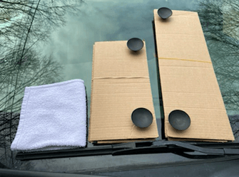 A cardboard box and a towel are on the windshield of a car.