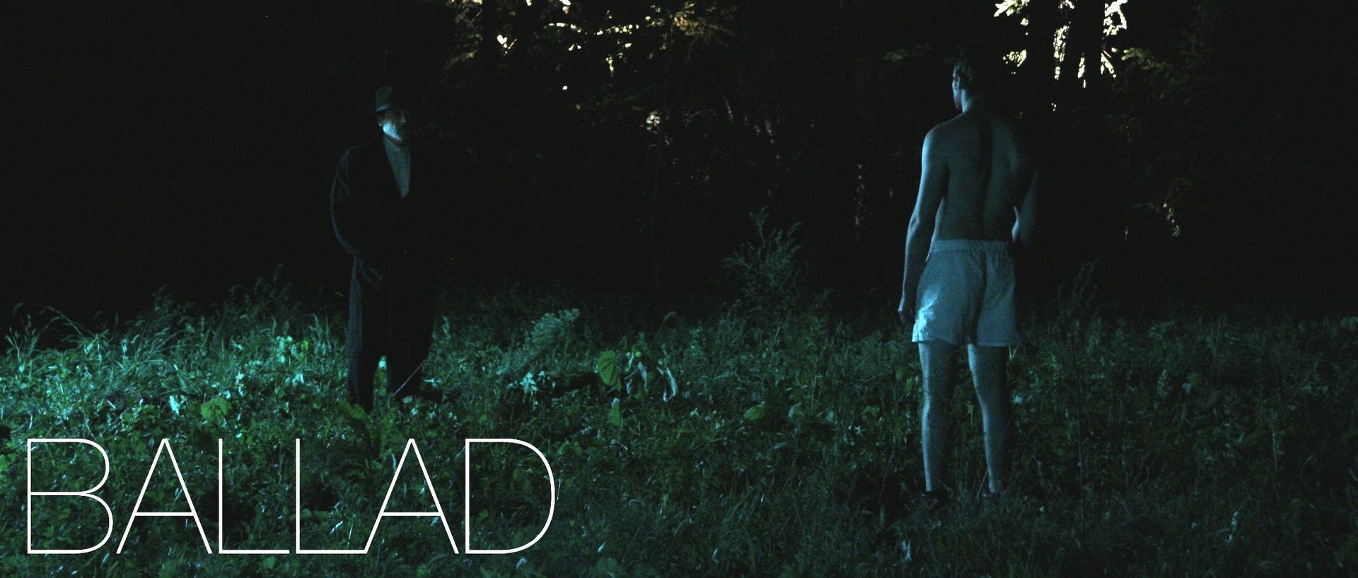 Two figures in a field at night, facing each other. One is shirtless in shorts.