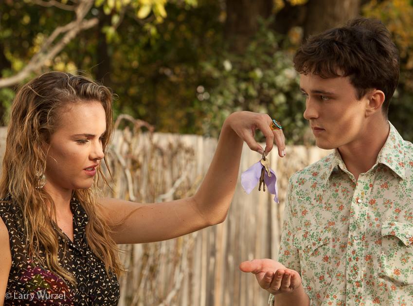 Woman handing keys to a man outside. She's looking sternly, he's looking concerned.