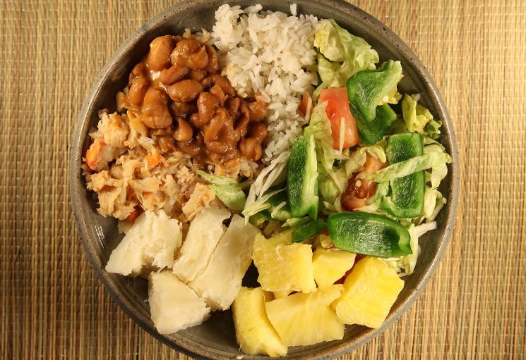 A bowl of food: white rice, beans, vegetables, pineapple, and cooked root vegetables.
