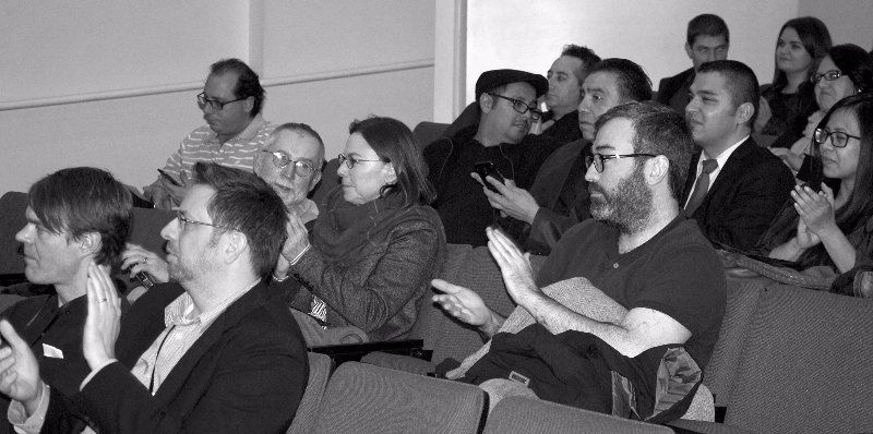 Audience clapping in a lecture hall. Several people are smiling and wearing casual attire.