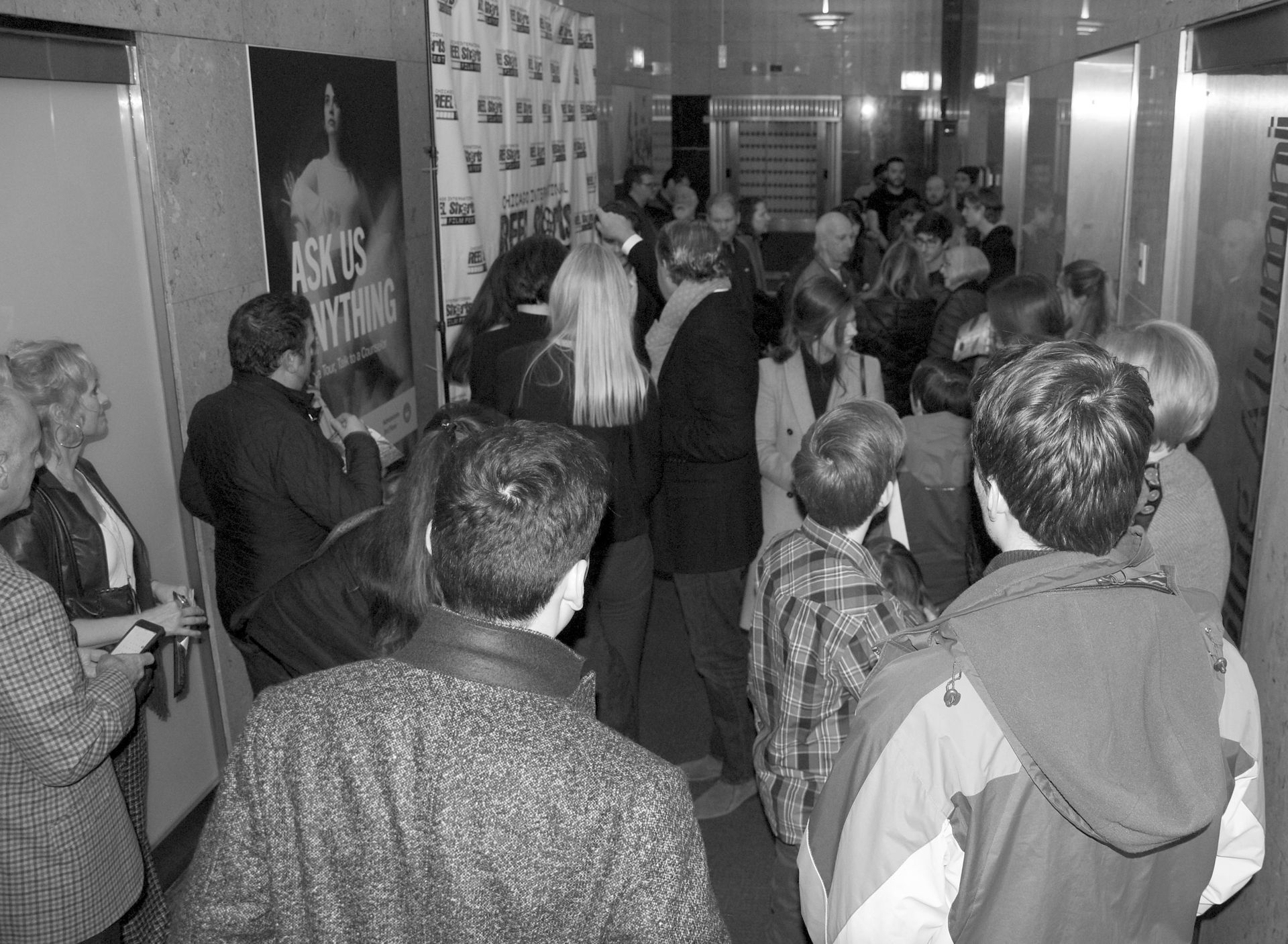 People crowded in a hallway; red carpet event, movie posters visible on wall.