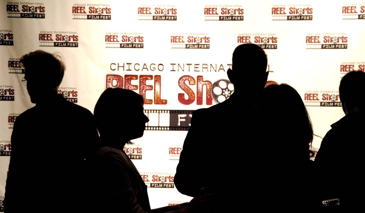 Silhouetted figures stand before a banner for the Chicago International Reel Shorts Film Festival.