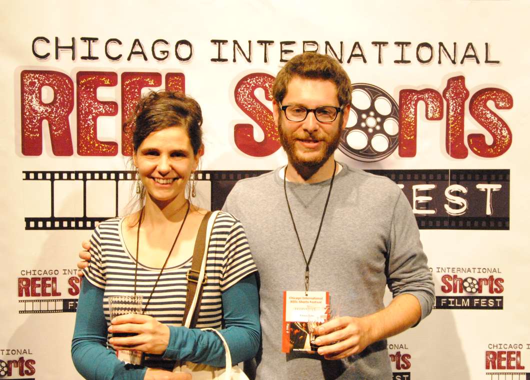 Woman with dark hair and man with beard, at Chicago film festival. Both smiling, holding drinks and lanyards.