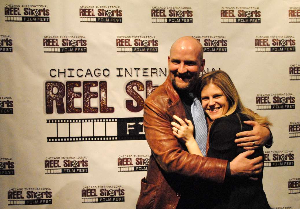 Man in brown jacket hugs a woman at a 