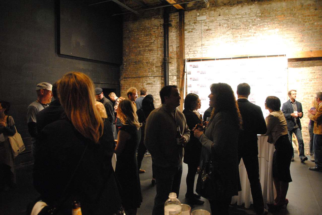 People at a social gathering in a brick-walled room, near a large white screen.