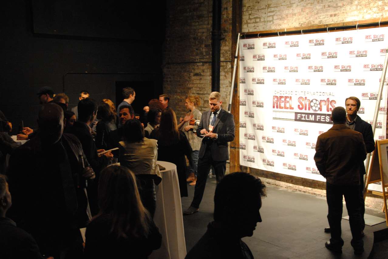 People at a film festival event with a step-and-repeat banner and brick wall.