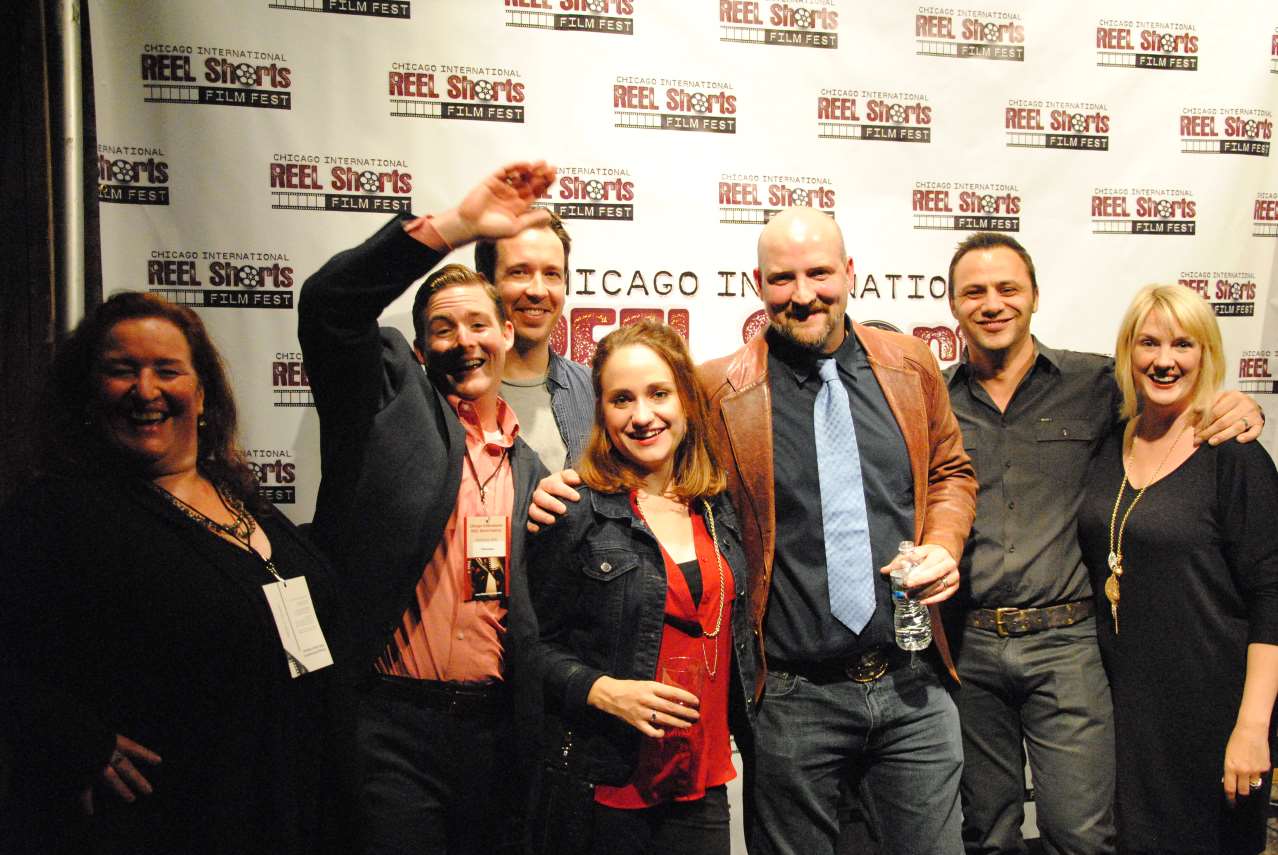 Group of people posing in front of a banner. Smiling, some with arms raised.