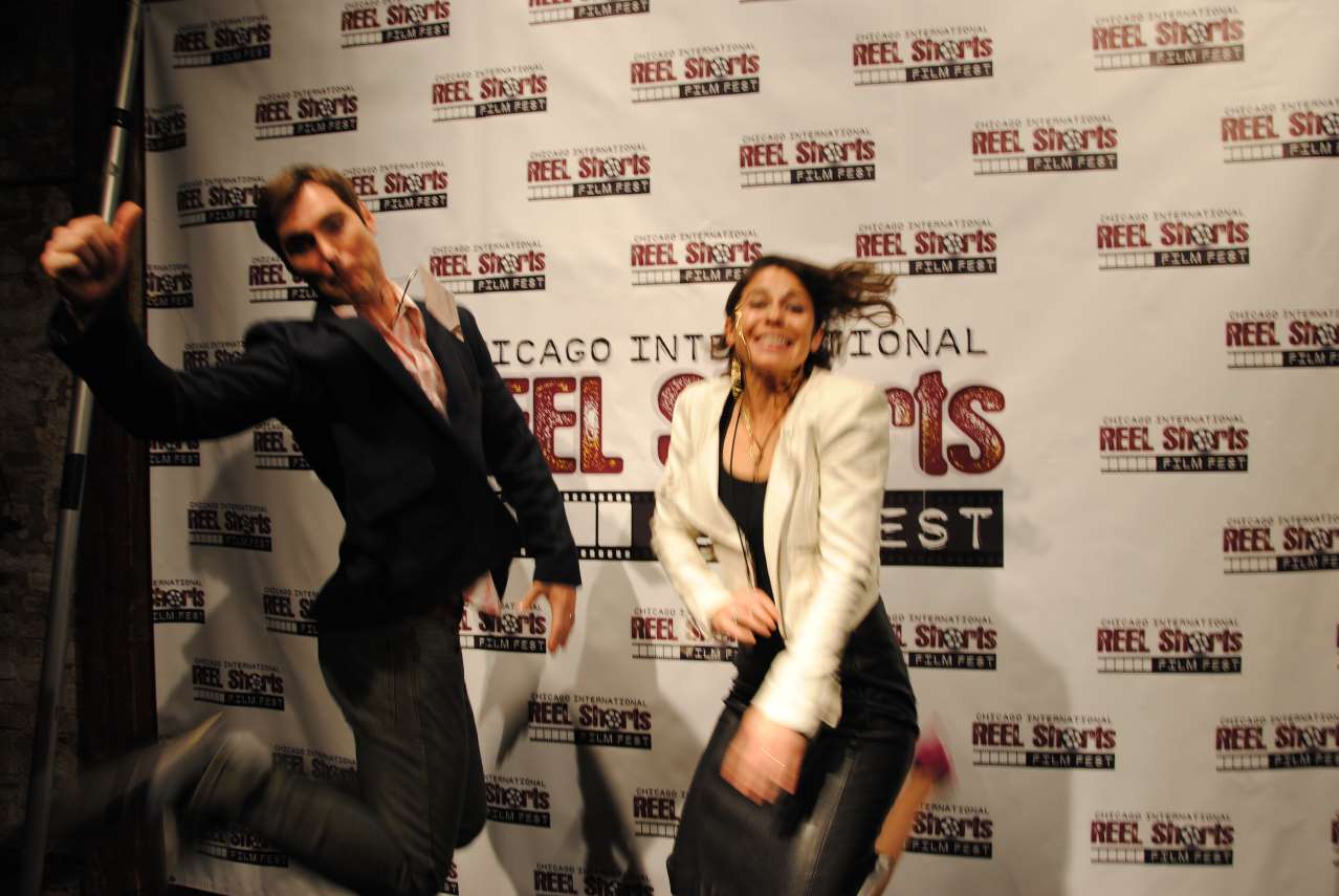 Man and woman jumping in front of a backdrop for Reel Shorts Fest; celebratory expressions.