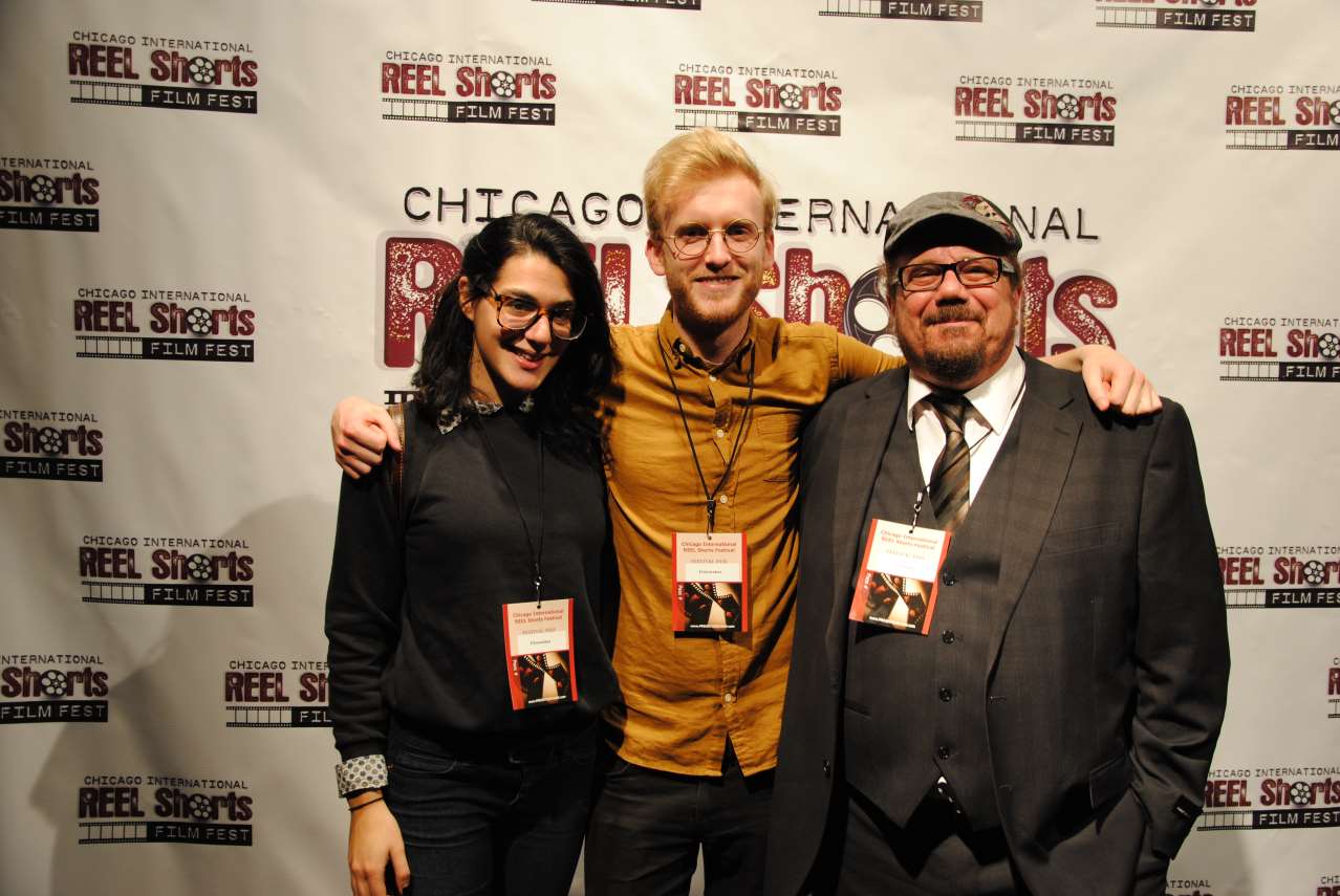 Three people smiling, posing for photo at Chicago film festival: woman, man with orange shirt, and man in suit.