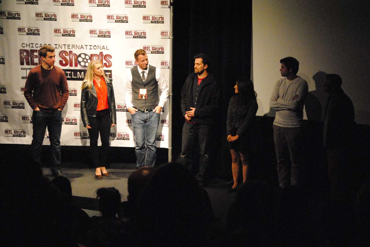 Film crew on stage at a screening: six people standing in front of a backdrop.