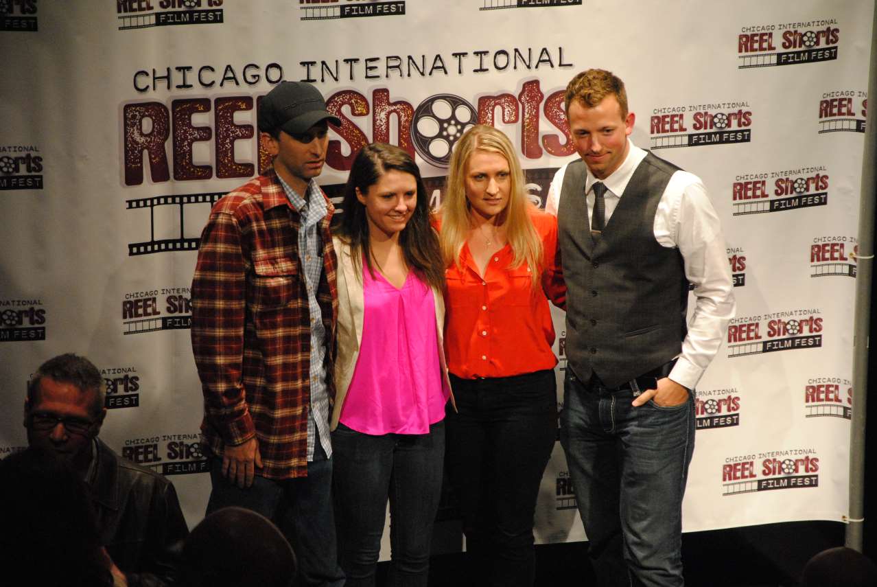 People pose at the Chicago International REEL Shorts event. A woman in red stands between two others, all smiling.