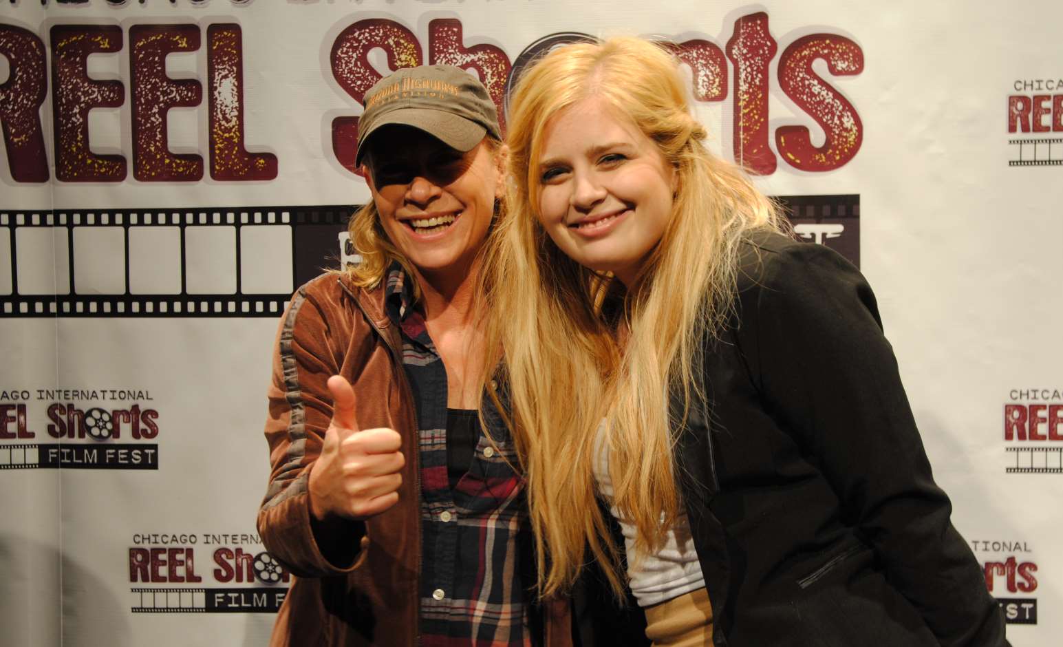 Two women smiling at a film festival. One gives a thumbs up, the other has long blonde hair.