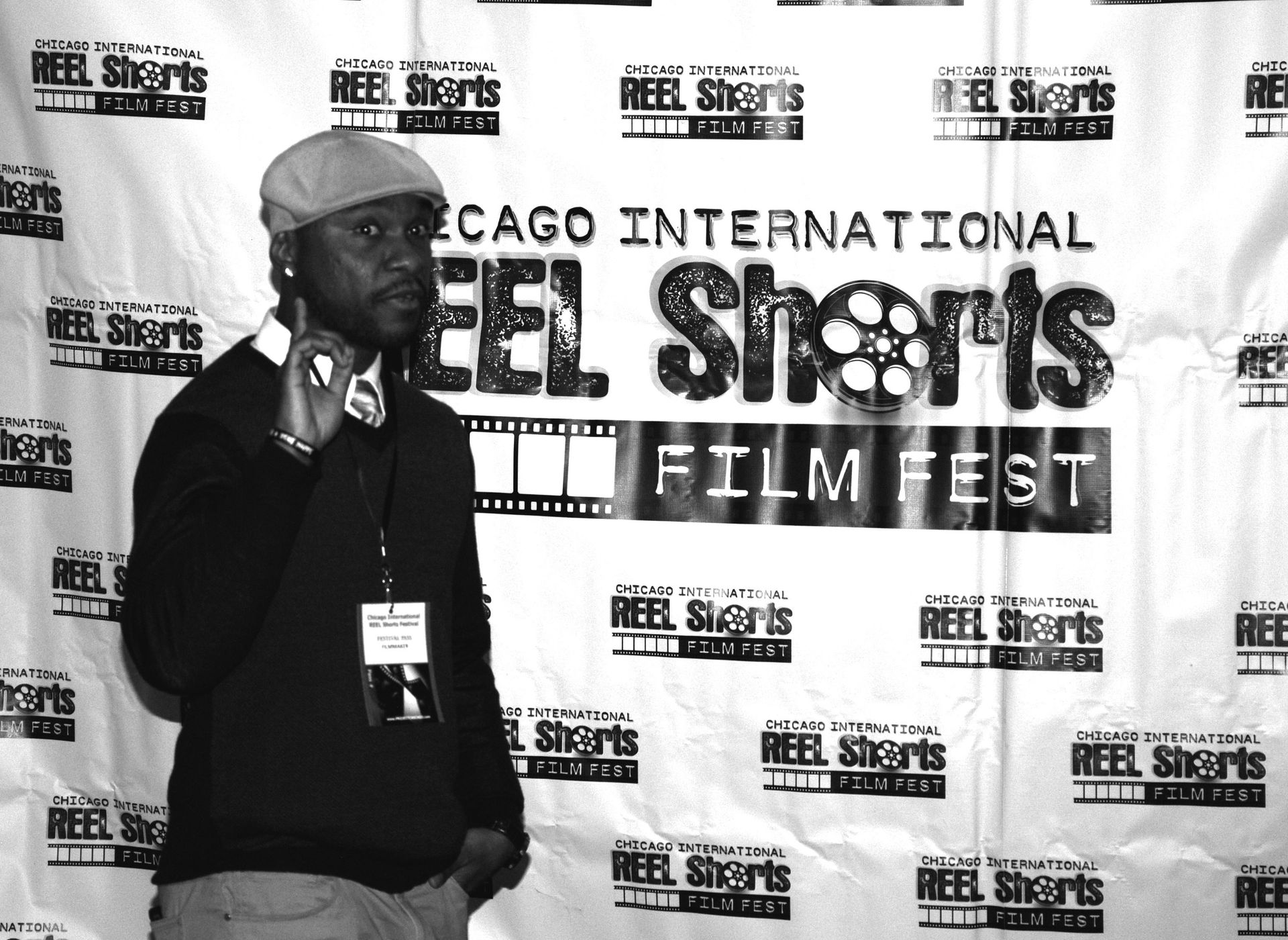 Man at the Chicago International Reel Shorts Film Fest, pointing up, wearing a cap and sweater, posing.