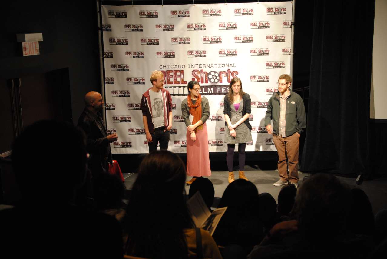 Filmmakers on stage at a festival. A screen backdrop reads 