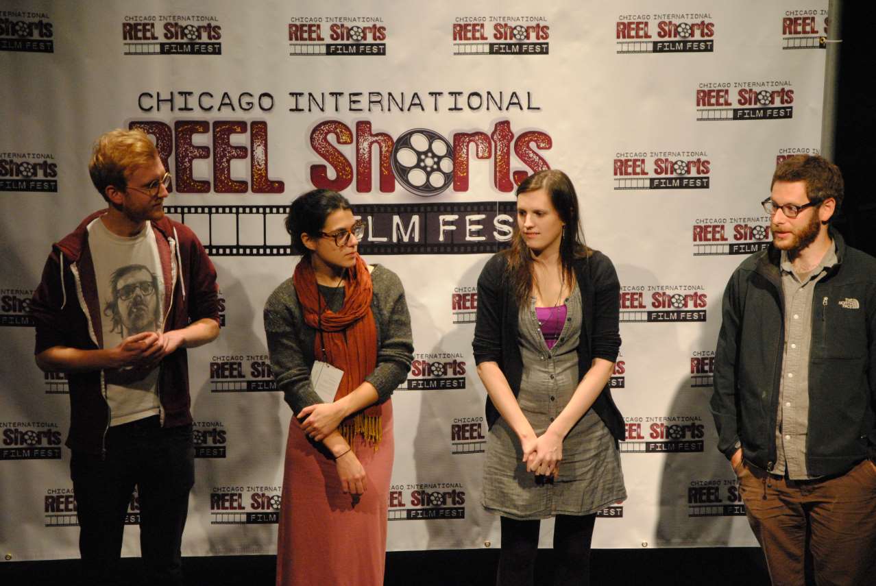 Four people on a stage with a backdrop. Two women and two men, standing in front of a 