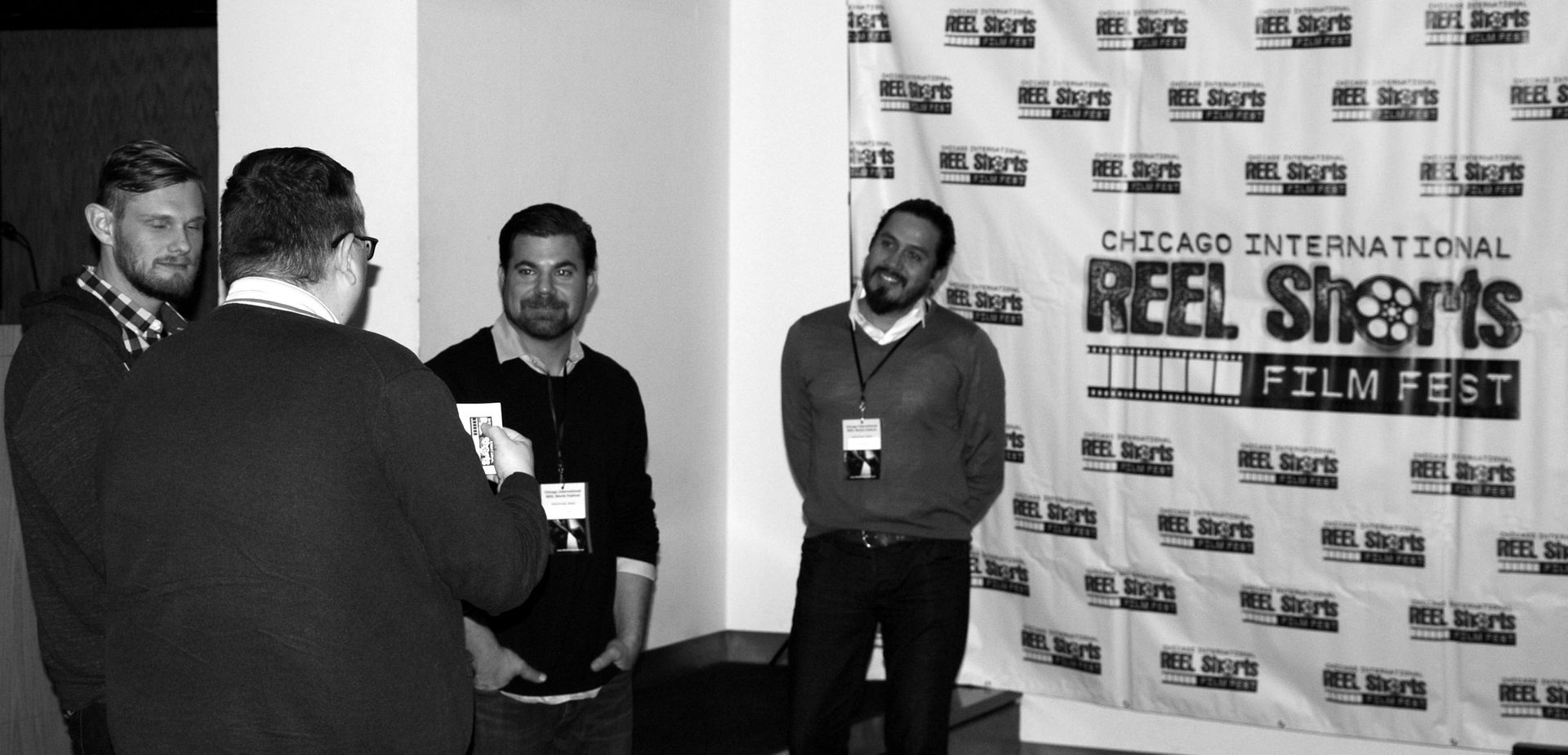 Four men at the Chicago International Reel Shorts Film Fest. One man in front, others talking near banner.
