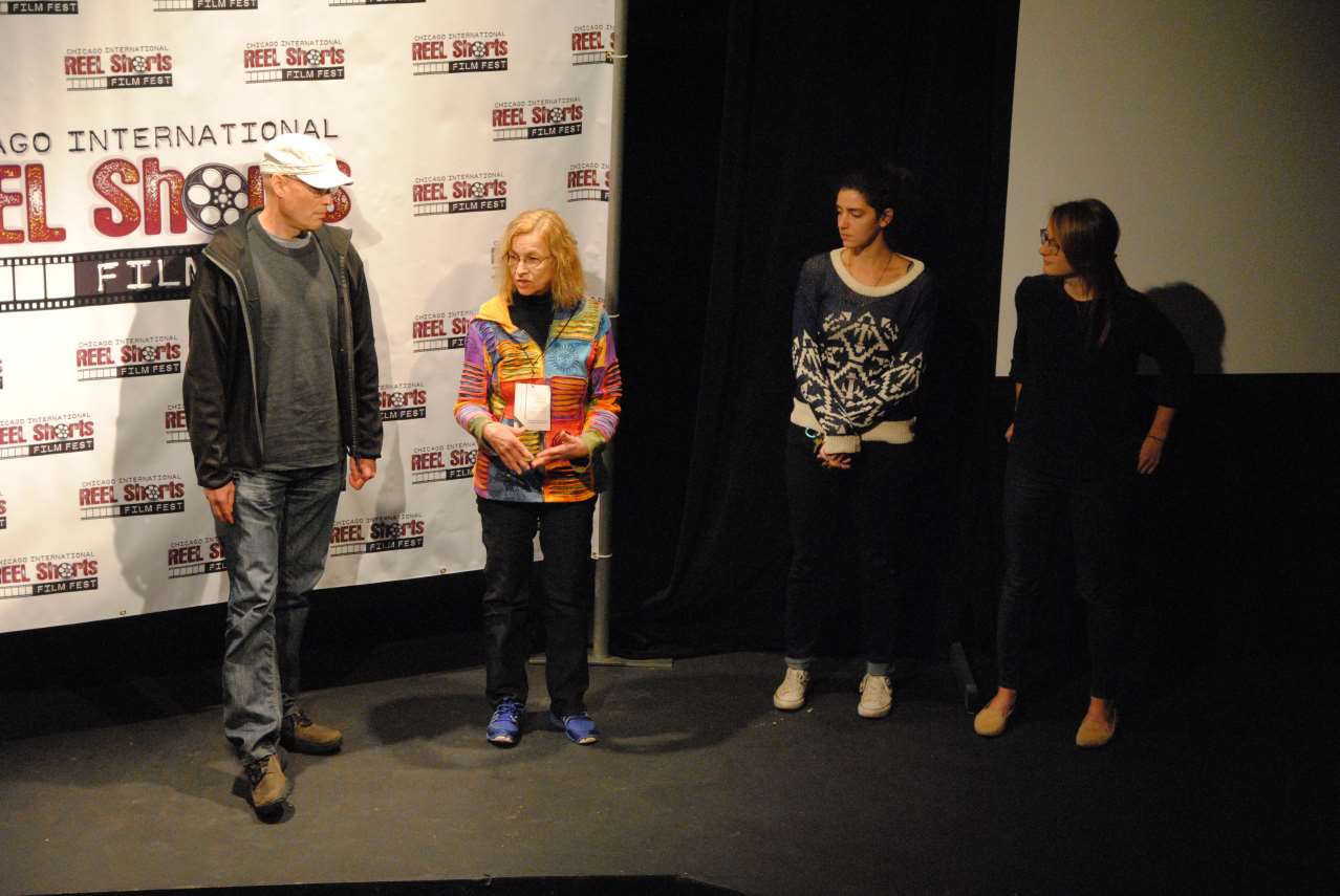 Four people on stage in front of a backdrop. A man, a woman in a colorful jacket, and two other women.
