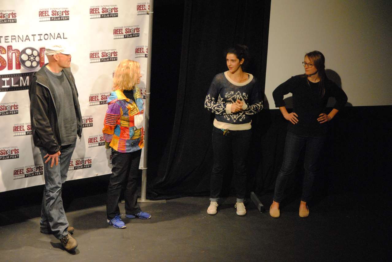 Four people on stage: two women, two men. One woman speaks, another has hands on hips.