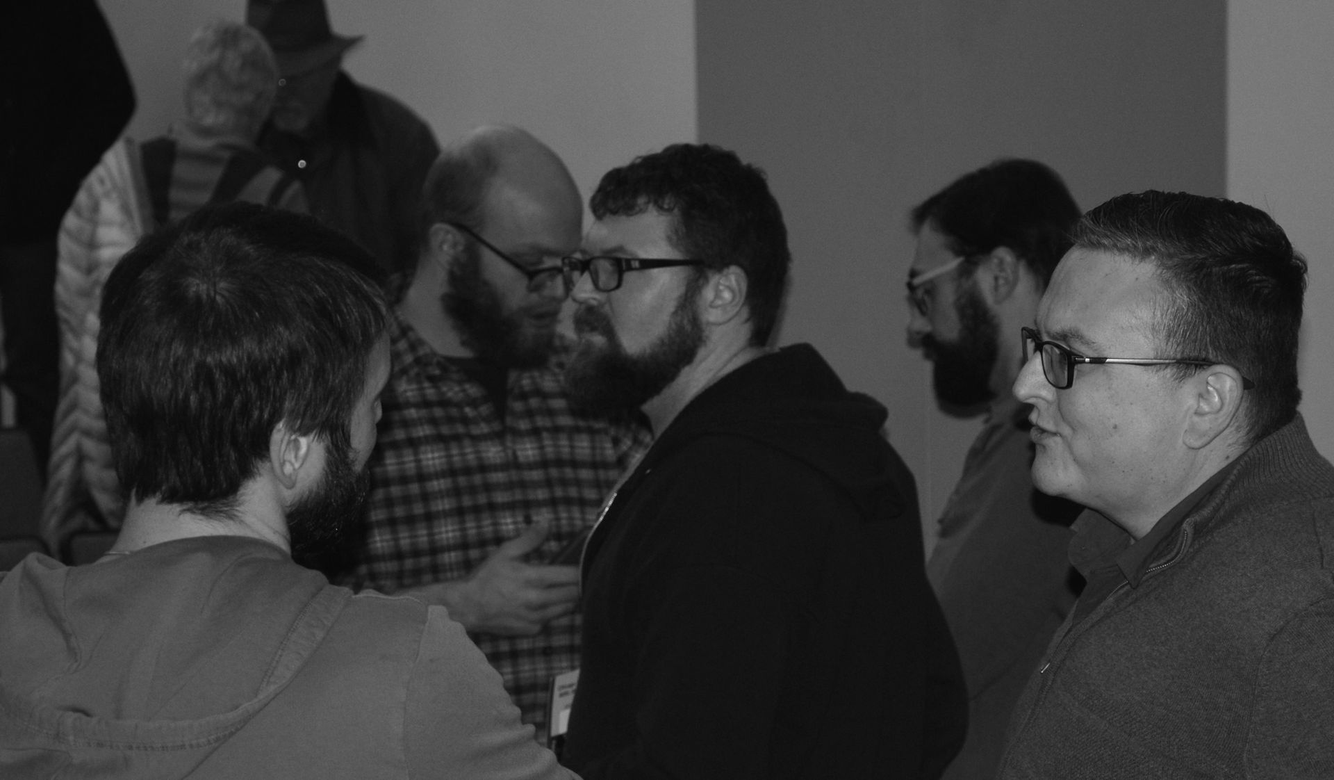 A group of men with beards and glasses talking in a room.