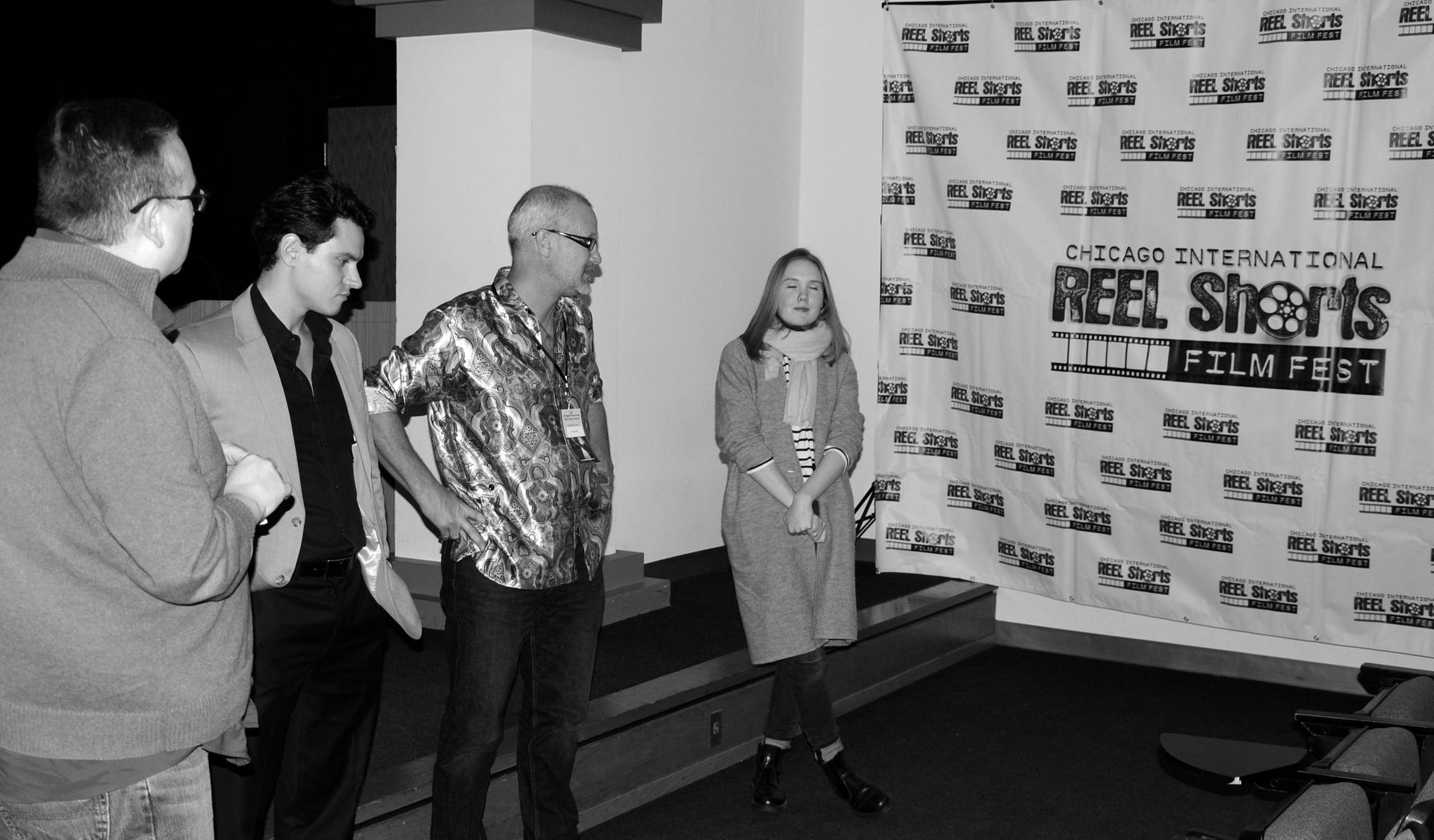 Group of people at film festival, posing in front of banner. One woman and three men. Black and white photo.