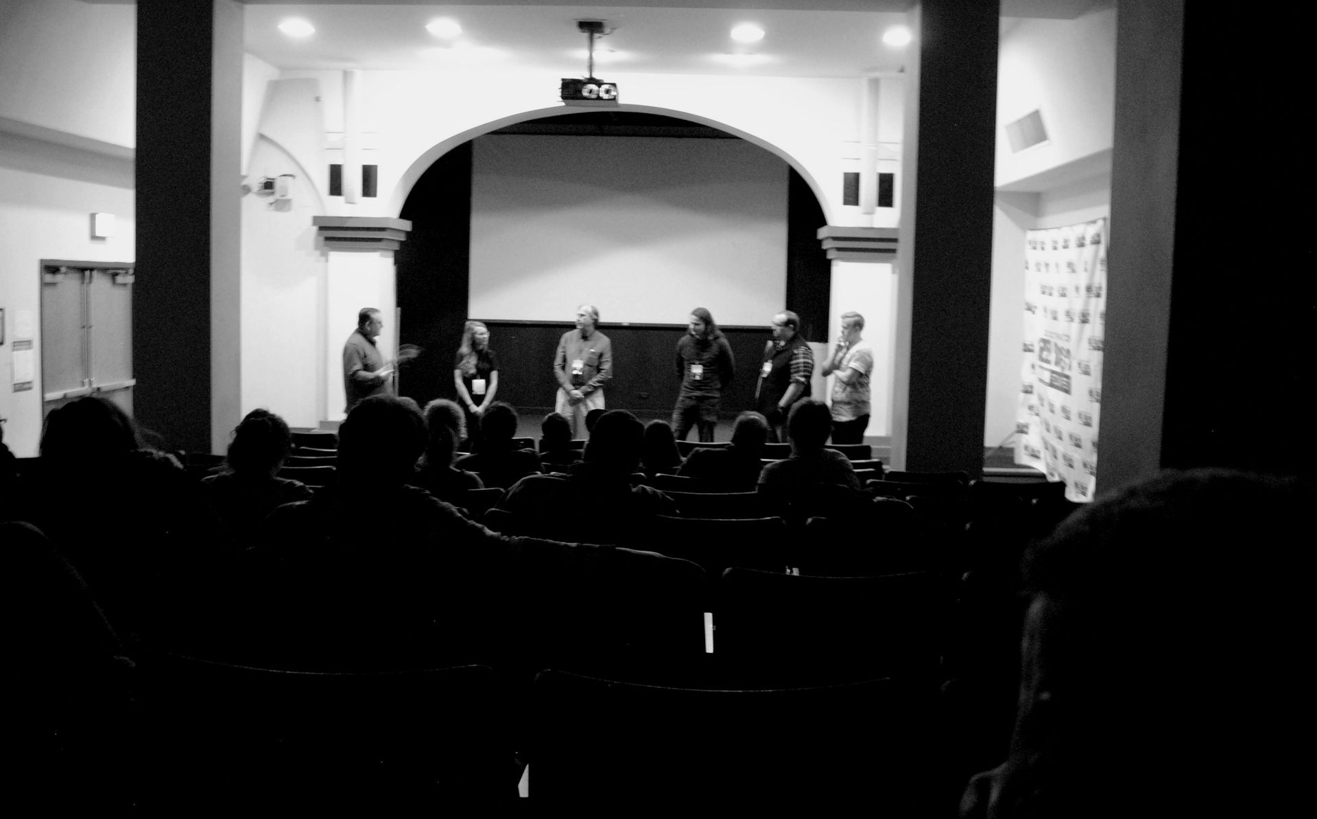 Panel discussion on stage at a theater; audience in the foreground. Black and white photo.