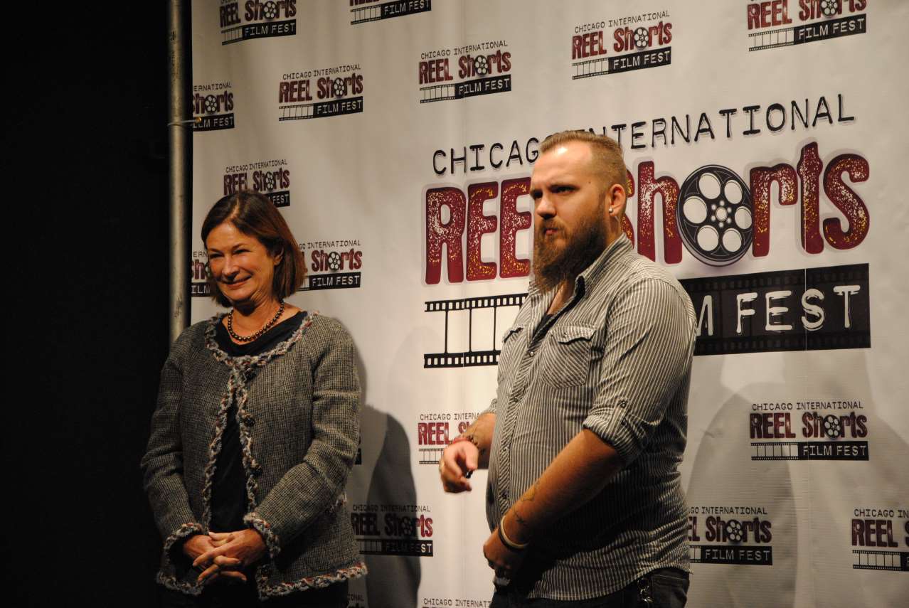 A woman and a man with a beard stand in front of a banner for Chicago International Reel Shorts Film Fest.