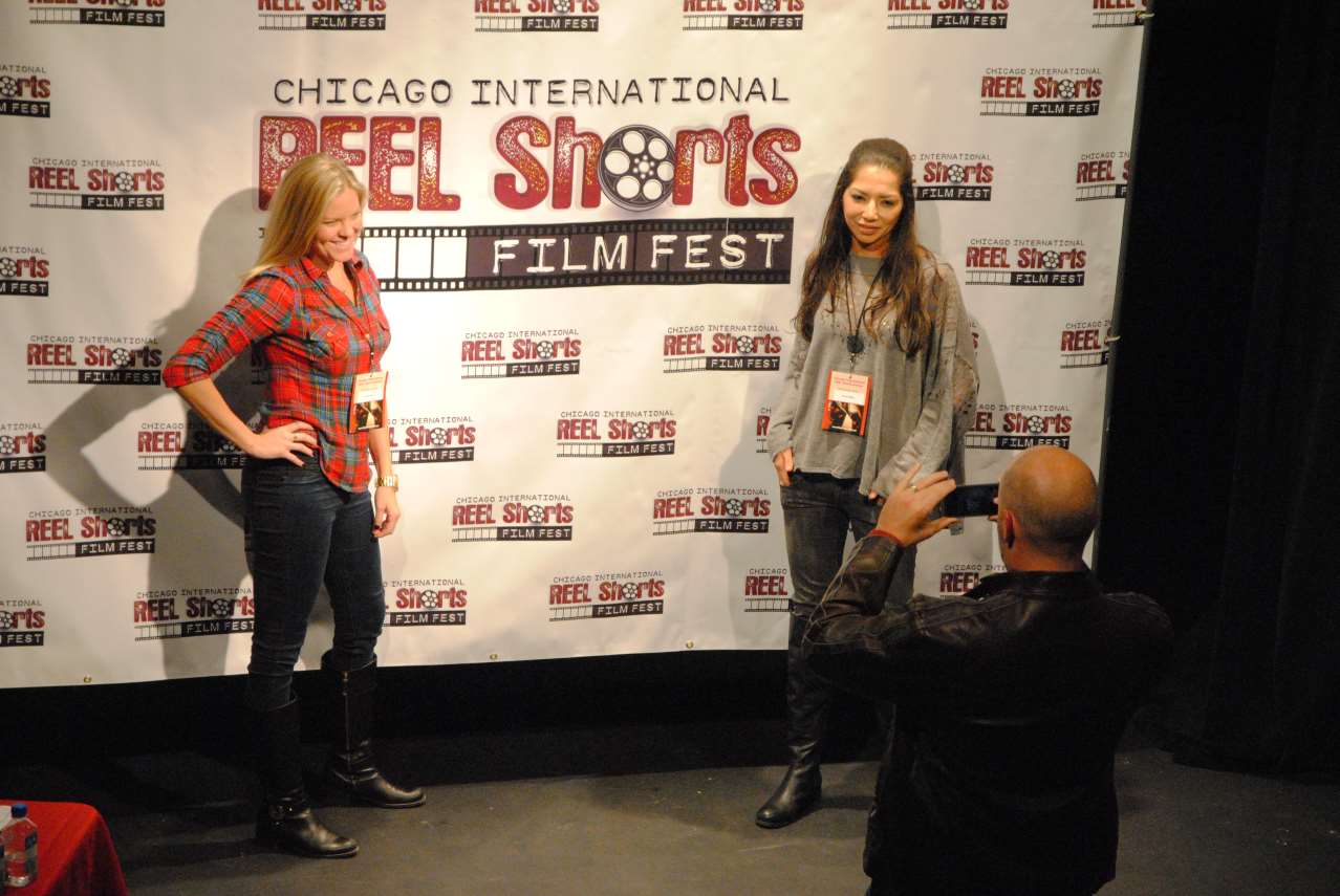 Two women posing for a photo in front of a Chicago film festival banner. Man takes their picture.