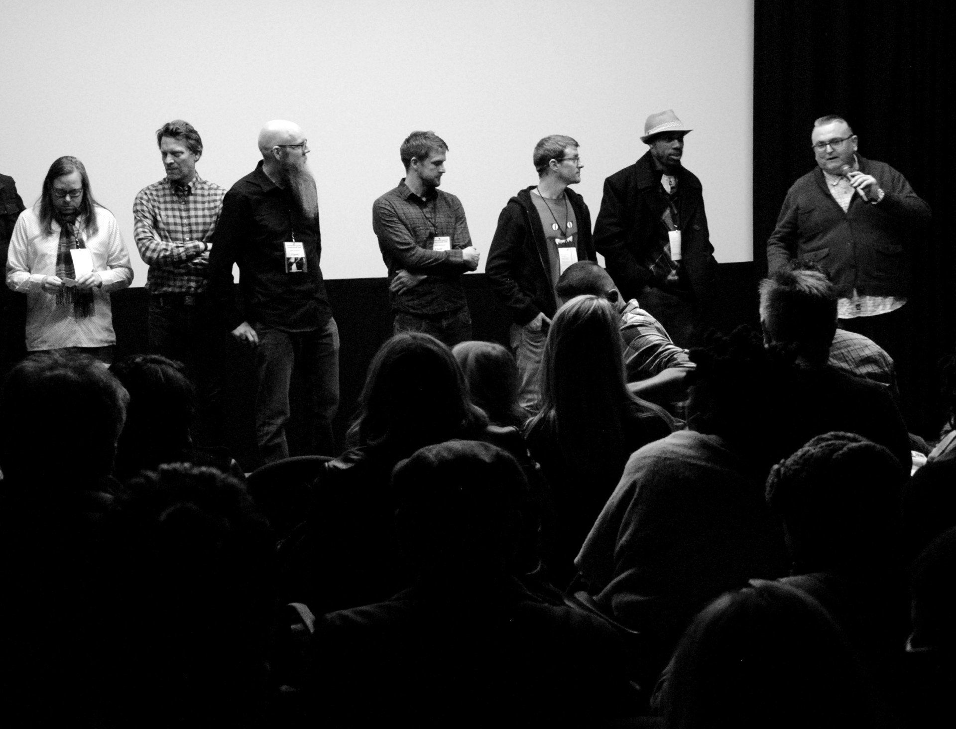 Panel of people on a stage in front of an audience, addressing them at an event. Black and white photo.