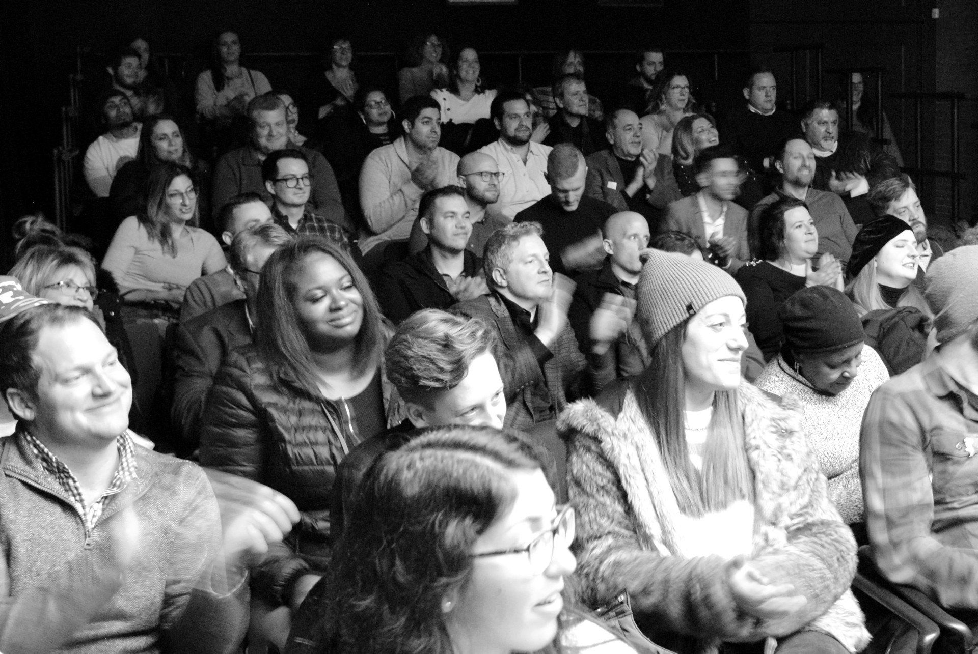 Audience in a dark theater, watching something, smiling, applauding.