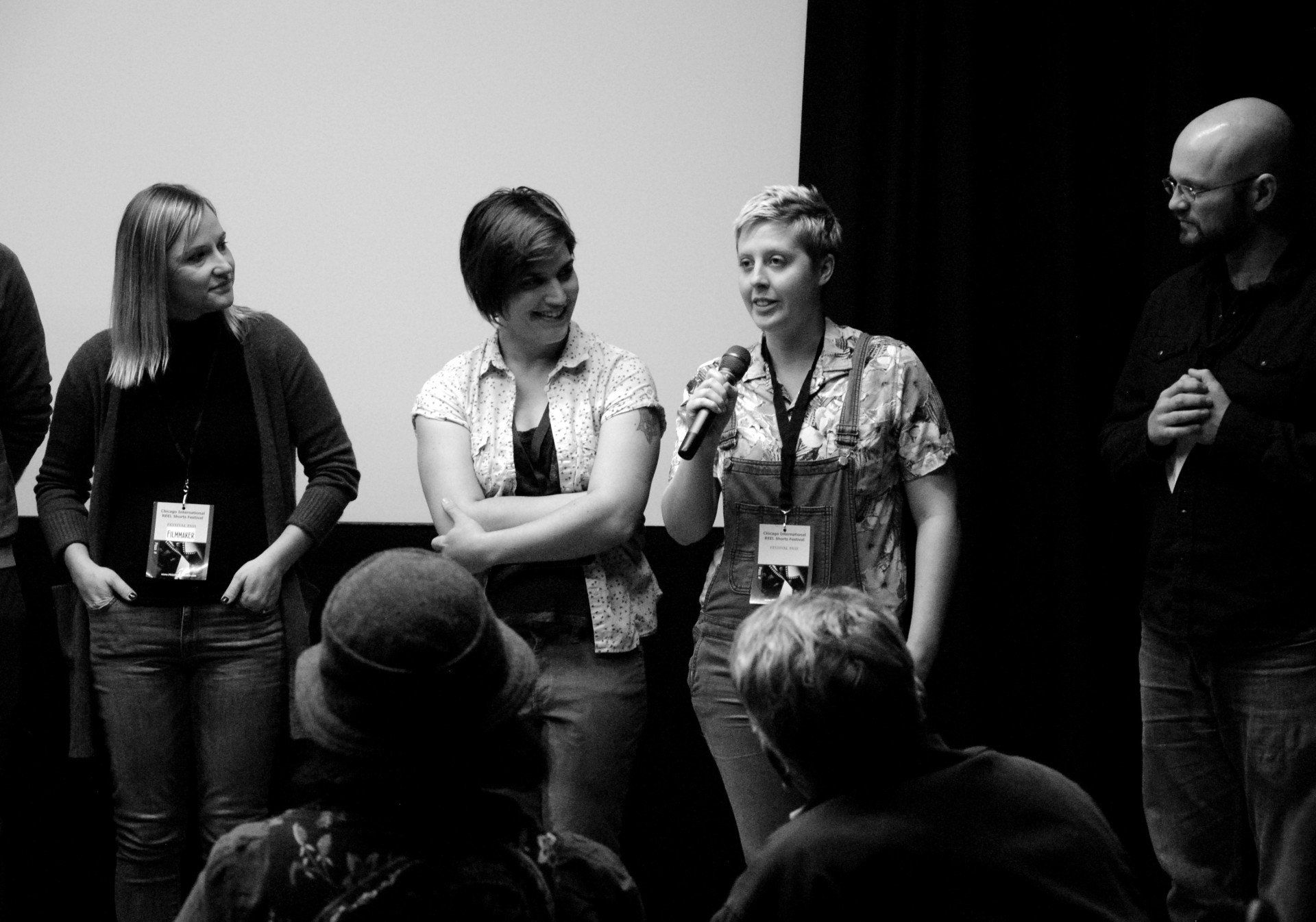 Panel of four people on stage with microphones and audience. Black and white.